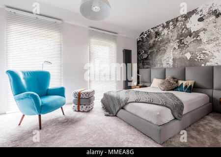 Monochromatic gray bedroom with grunge wall, wooden bedside table, white walls and blue vintage style armchair Stock Photo