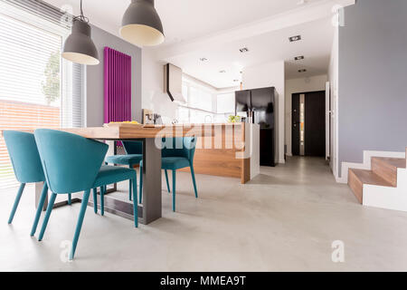 Monochromatic modern open plan apartment with colorful and wooden accents in dining room and kitchen with stairs and door entrance Stock Photo
