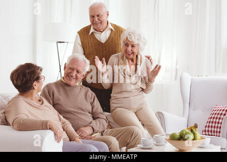 Group of mature friends talking and smiling in light room Stock Photo