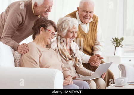 Group of seniors using laptop, sitting in light room Stock Photo