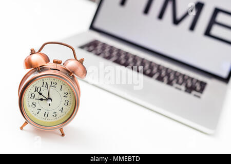 office table with time on screen laptop, and vintage alarm clock on white background Stock Photo
