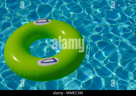 Green life ring floating on blue water in the swimming pool Stock Photo