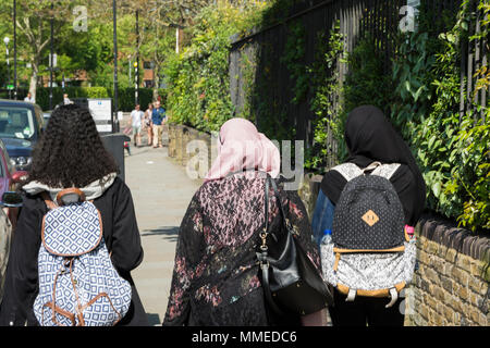 Back of headshot of three young women wearing hijab headscarves walking down a street in Chelsea, London, UK Stock Photo