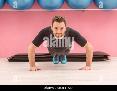 Portrait of a young handsome man doing pushups in a gym. Stock Photo