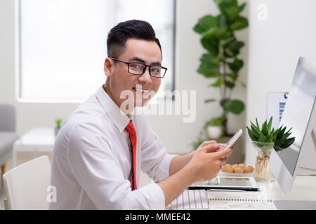 Man using computer and smart phone at the table in office against the window Stock Photo