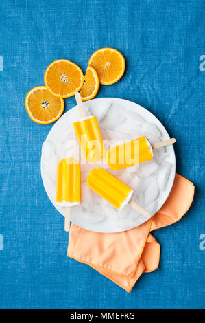 orange popsicles on a blue table cloth with orange slices Stock Photo