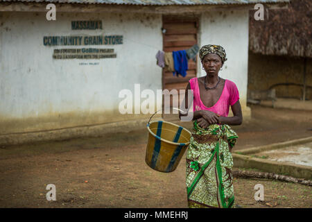 YONGORO, SIERRA LEONE - June 06, 2013: West Africa, unknown woman with a bucket next to the grain warehouse in the village of huts near the capital Fr Stock Photo