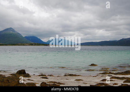 View on a bay between the fjords in Lofoten, Norway. The water colors turquoise due to the white sands. Dramatic overcast sky. Stock Photo