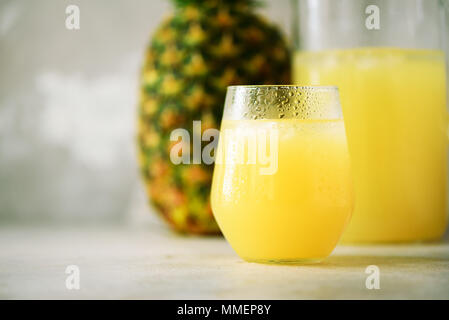 Glass of pineapple smoothie and whole fruit on gray background. Copy space. Summer, holiday concept. Raw, vegan, vegetarian, clean eating diet Stock Photo