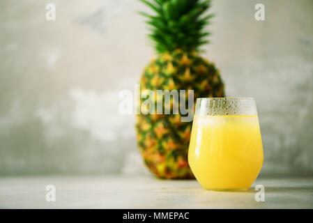 Glass of pineapple smoothie and whole fruit on gray background. Copy space. Summer, holiday concept. Raw, vegan, vegetarian, clean eating diet Stock Photo