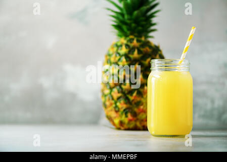 Glass jar of pineapple smoothie and whole fruit on gray background. Copy space. Summer, holiday concept. Raw, vegan, vegetarian, clean eating diet Stock Photo