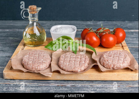 Chicken burgers cutlets on a wooden board with cherry tomatoes and spices Stock Photo
