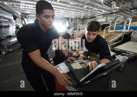 USS Carl Vinson (CVN-70) is a Nimitz-class nuclear-powered aircraft carrier commissioned in 1982. The archival image records aviation support personnel using a Portable Electronic Maintenance Aid system within the hangar bay during sustainment training operations in the Pacific Ocean in 2017. Stock Photo