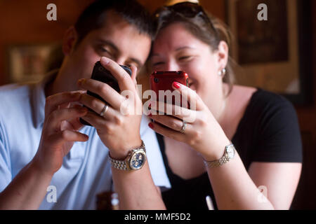 Millennial couple with their heads together, looking at their iPhones. Stock Photo