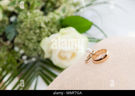 Wedding rings on pillow / pin cushion with flowers in background Stock Photo