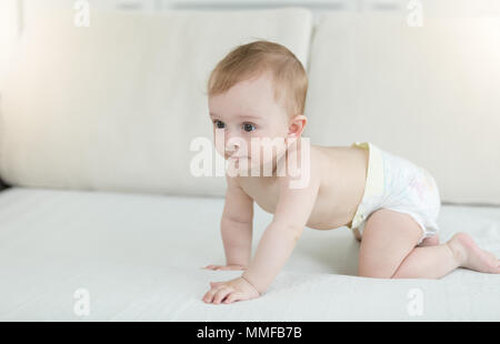Adorable 10 months old baby boy in diapers crawling on bed Stock Photo