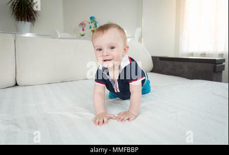 Portrait of cute smiling baby boy crawling on bed and looking in camera Stock Photo