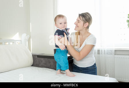 Portrait of happy smiling mother holding her baby son standing on sofa Stock Photo