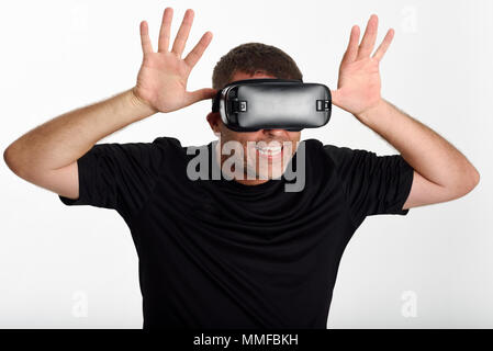 Man looking in VR glasses and gesturing with his hands. Beautiful surprised guy wearing virtual reality goggles watching movies or playing video games Stock Photo