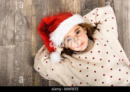 Adorable little girl wearing santa hat laying on wooden floor. Winter clothes for Christmas Stock Photo