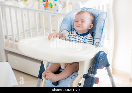 10 months old baby boy sitting in highchair and crying Stock Photo