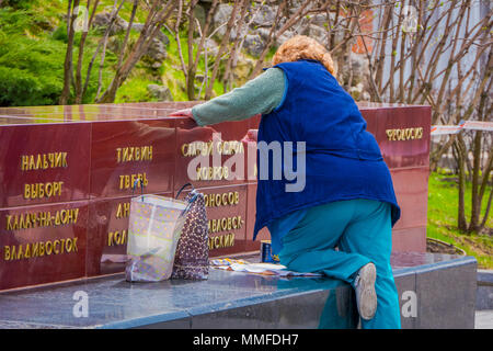 MOSCOW, RUSSIA- APRIL, 29, 2018: Outdoor view of eldery woman wearing blue jacket in the park painting with golden color the letters of outdoor structure on red square in Moscow Stock Photo