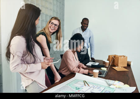 Diverse group of work colleagues smiling and having a discussion together around a desk in a modern office Stock Photo