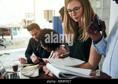 Focused businesspeople discussing paperwork while working together in a modern office with colleagues in the background Stock Photo