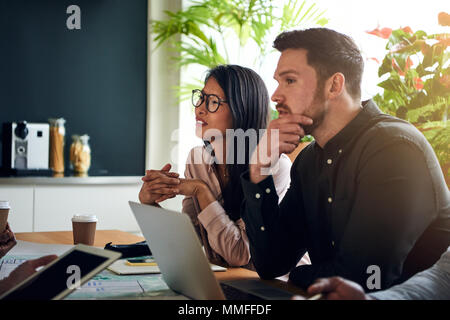 Diverse coworkers talking while sitting together at a boardroom table in an office having a meeting Stock Photo
