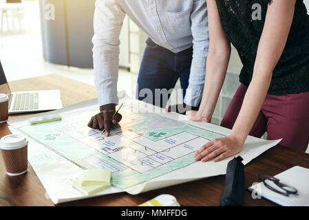 Two architects standing together in a modern office leaning over a desk discussing a building design Stock Photo