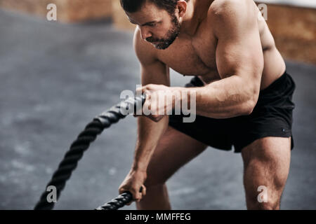 Fit young man in sportswear looking focused while exercising with ropes during an workout session at the gym Stock Photo