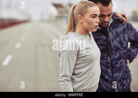 Diverse young couple standing on a road looking focused while preparing for a run together on an overcast day Stock Photo