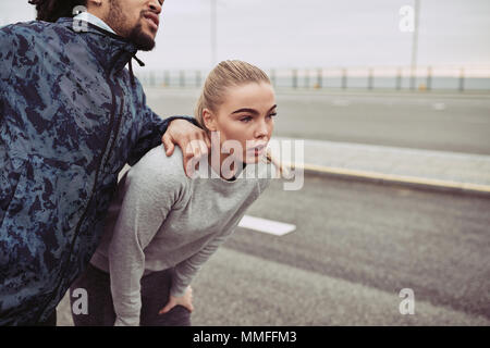 Diverse young couple in sportswear taking a break together before going for a run outside on an overcast day Stock Photo