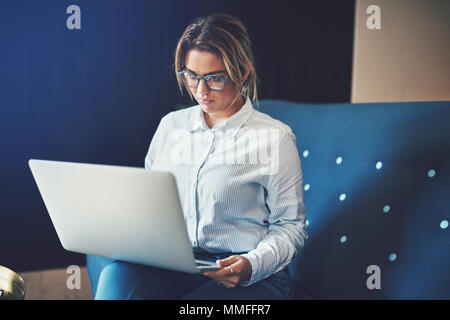 Young businesswoman wearing glasses working online with a laptop while sitting on a sofa at home Stock Photo