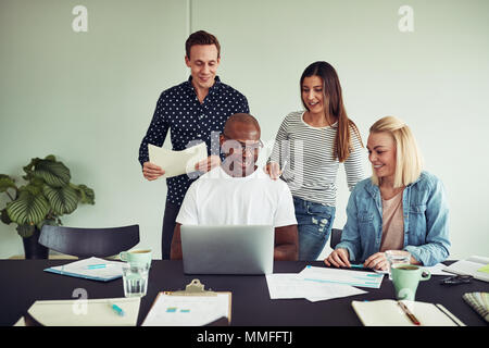 Diverse group of smiling businesspeople discussing paperwork and using a laptop while working together in an office Stock Photo