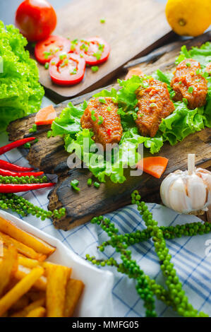 Fried chicken wings with spicy chilli sauce on rustic serving board, herbs and vegetable over wooden background. Stock Photo