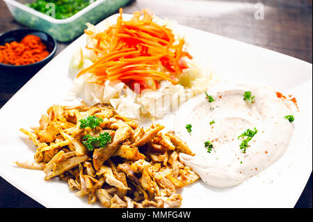 Chicken Shawarma or Doner Kebab serving with hummus and vegetable in white plate on wooden table. Stock Photo