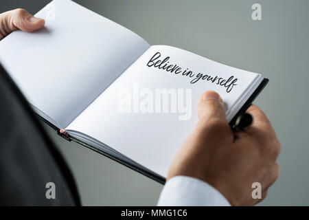 closeup of a young caucasian man in an elegant suit with a notebook in his hands with the text believe in yourself written in it Stock Photo