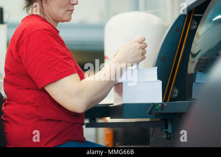 Hands of female worker with a stacks of paper in front of printing machinery equipment Stock Photo