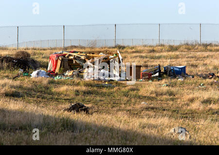 Homeless Camp against cyclone fence, dry grass, hillside. Stock Photo