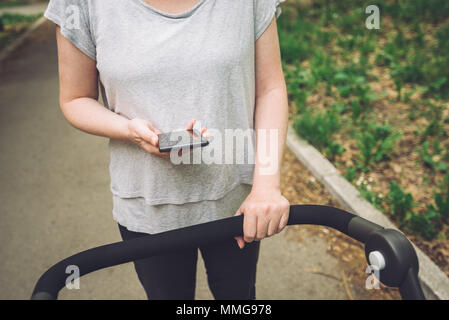 Mother pushing baby stroller and reading text message on smart phone while walking on the street in casual sport clothing Stock Photo