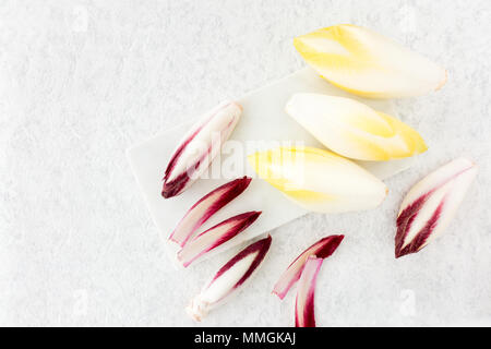 Whole chicory and red chicory leaves on a white marble chopping board. Top view. Stock Photo
