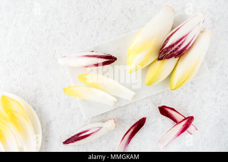 Whole chicory and chicory leaves on a white marble chopping board and white porcelain plate. Top view. Stock Photo
