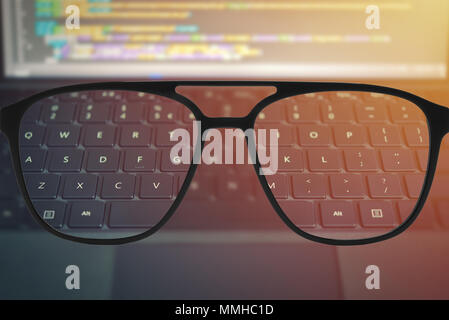 Clear image in glasses against blurry llaptop keyboard with code text on blurry screen Stock Photo