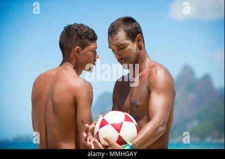 RIO DE JANEIRO - FEBRUARY 9, 2017: Young brazilian men stand on the beach with a football at Arpoador, against a skyline view of two brothers mountain Stock Photo