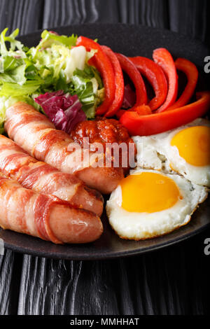 Delicious breakfast of fried sausages wrapped in bacon, eggs and fresh salad close-up on a plate on a table. vertical Stock Photo