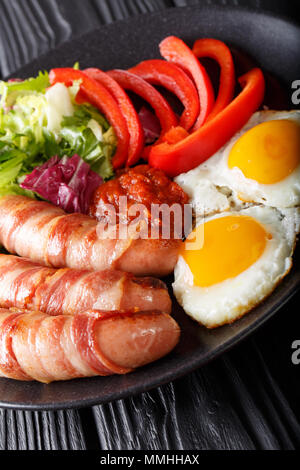 Fried sausages wrapped in bacon, eggs and fresh salad close-up on a plate. vertical Stock Photo