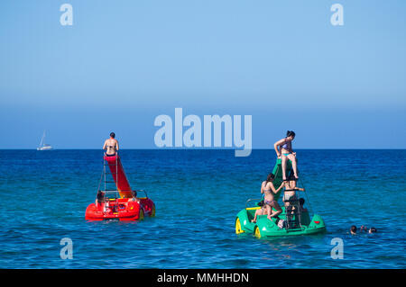 Young women riding colourful pedalos in the Mediterranean sea on a warm summer's day in Cala San Vicente, Mallorca, Spain. Stock Photo