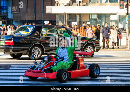 Tokyo, Shibuya crossing. Popular tourist activity, driving MariCar, Mario kart while dressed as Mario character. Woman waving, driving, eye-contact Stock Photo