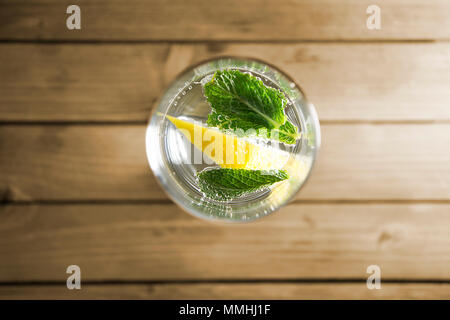 Piece of lemon and mint leaf in transparent glass of mineral water with bubbles on wooden background Stock Photo